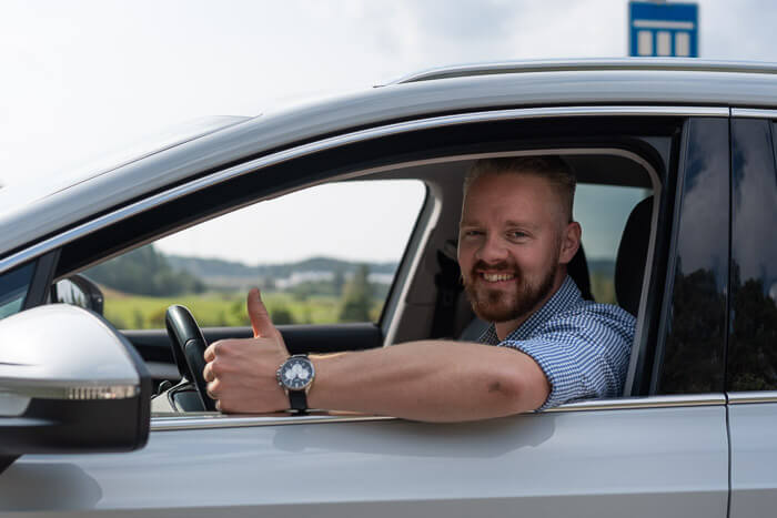 Mies istuu autossa ja näyttää peukaloa ylöspäin.